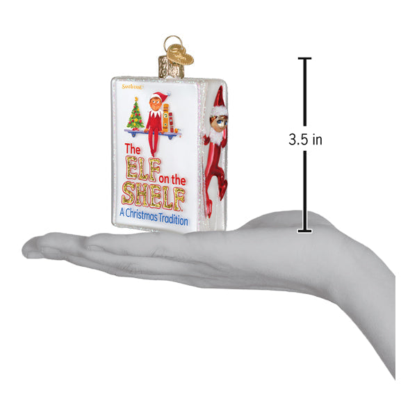 The Elf on the Shelf book ornament on an open palm with a 3.5 inch height marker for scale