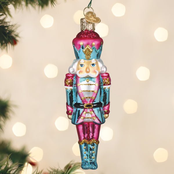 Pastel pink and aqua nutcracker glass ornament hanging on a lit Christmas tree