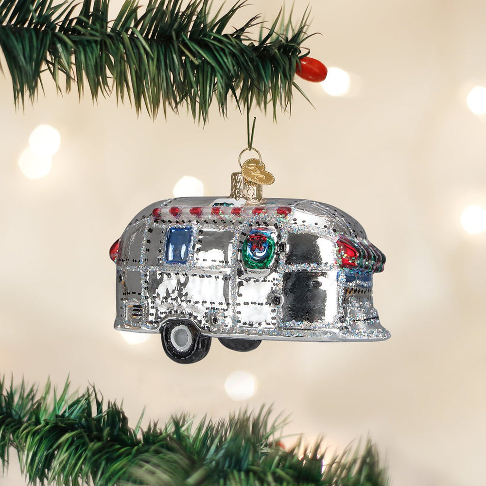 Silver vintage camper trailer ornament hanging on a green Christmas tree branch with soft lights