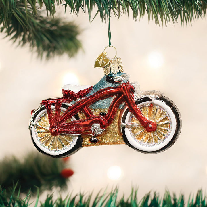 Red cruiser bike ornament hanging on a lit Christmas tree with warm bokeh lights