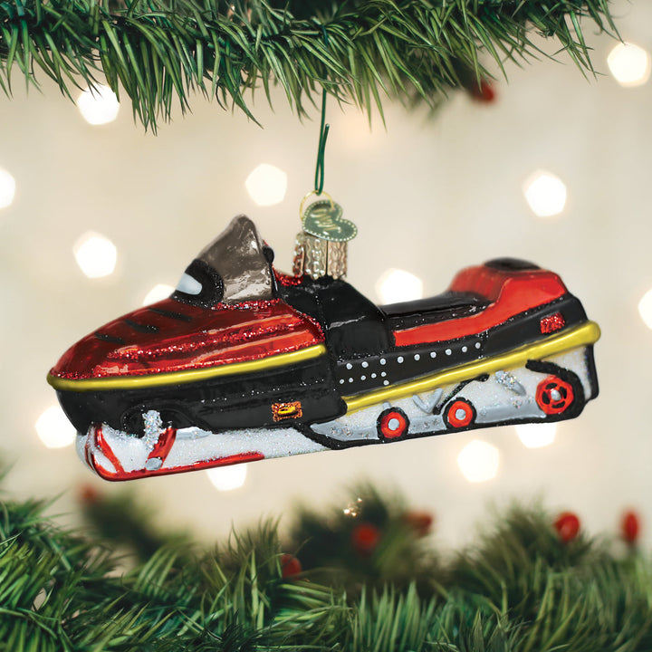Red snowmobile glass ornament hanging from a lit Christmas tree