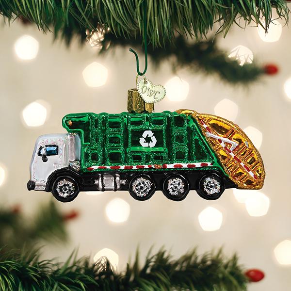 Garbage truck Christmas ornament hanging on a pine branch with soft holiday lights behind it