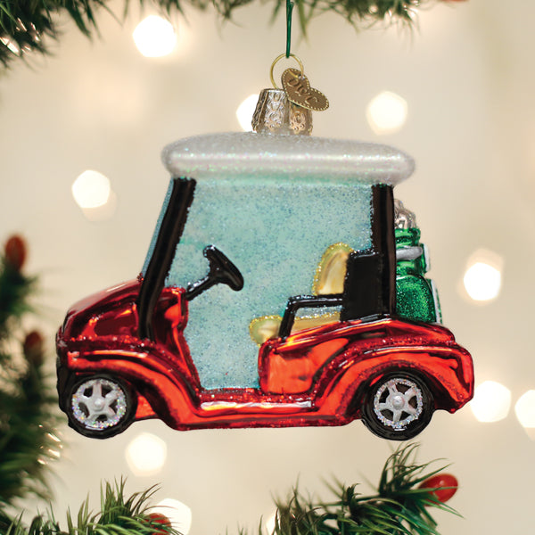 Golf cart Christmas ornament hanging on a pine tree beside a wrapped gift and warm lights