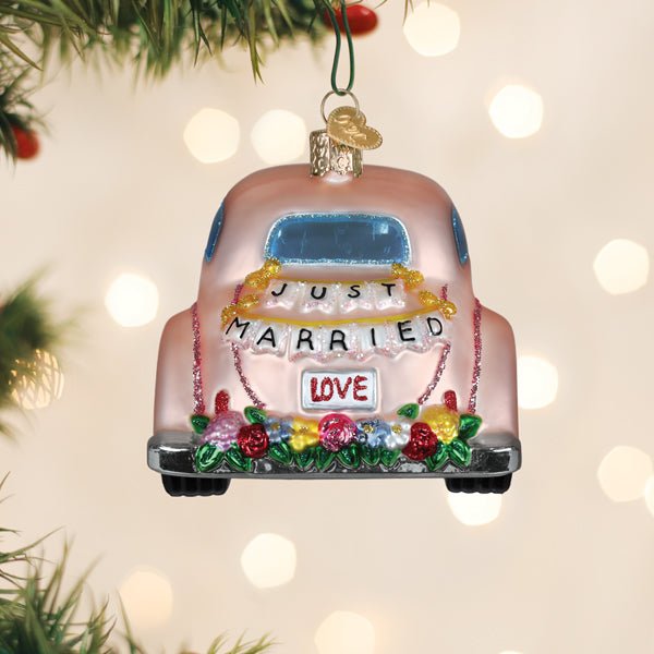 Just Married car ornament hanging on a Christmas tree with soft holiday lights