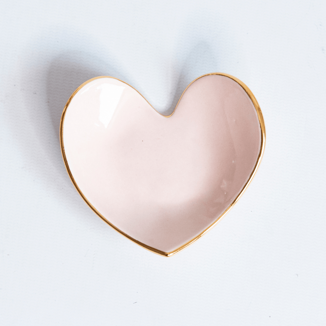Blush pink heart ring dish with a gold edge, shown from above on white