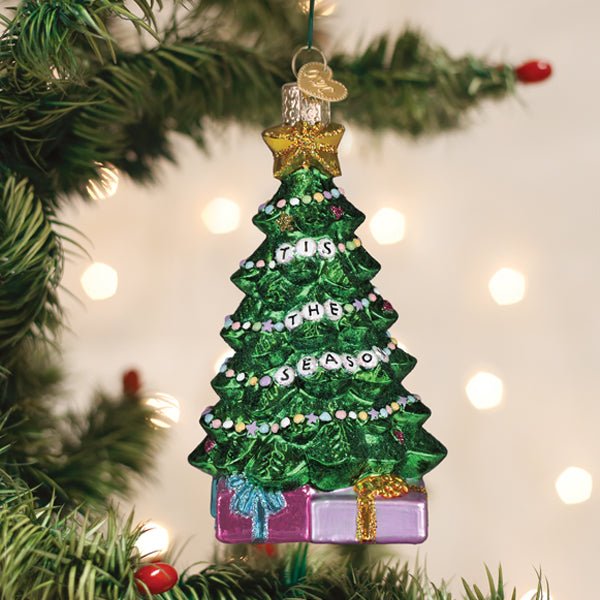 Friendship bracelet tree glass ornament with a gold bow hanging on a lit Christmas tree