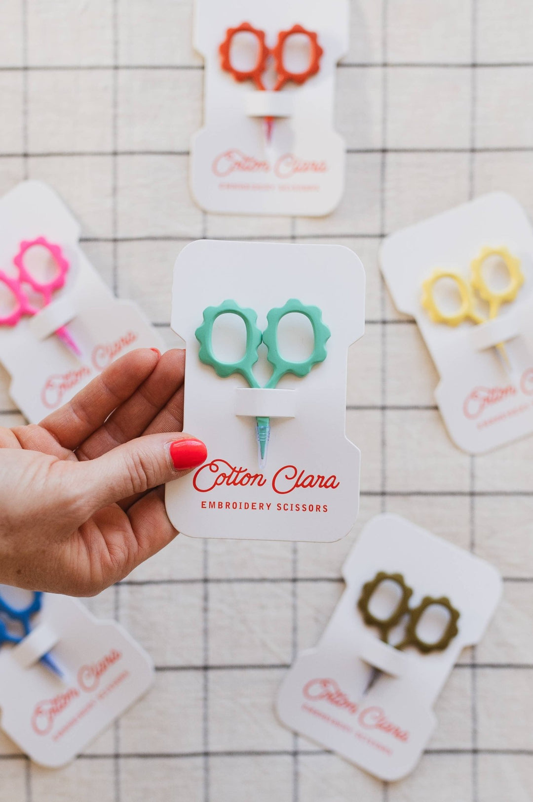 Hand holding the mint flower embroidery scissors card over a grid tablecloth