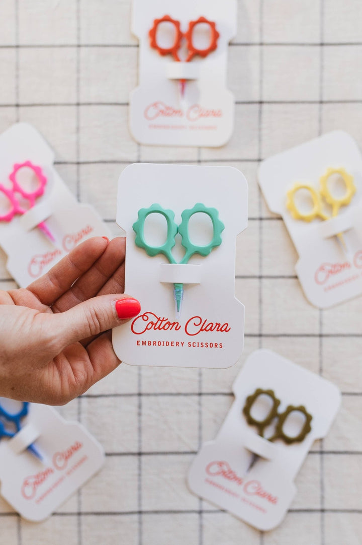 Hand holding the mint flower embroidery scissors card over a grid tablecloth