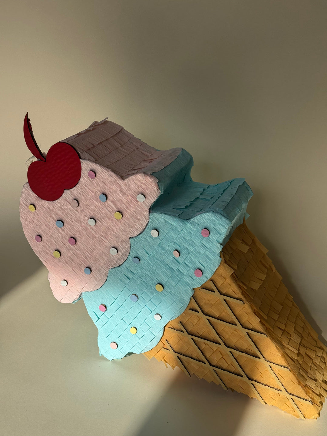 Pinata ice cream cone with a cherry on top against a neutral background