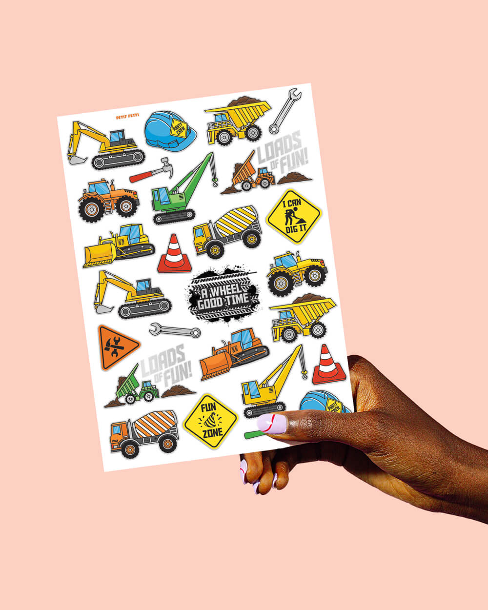 A hand holding one 8.25 by 6 inch sheet of construction tattoos with trucks and traffic signs