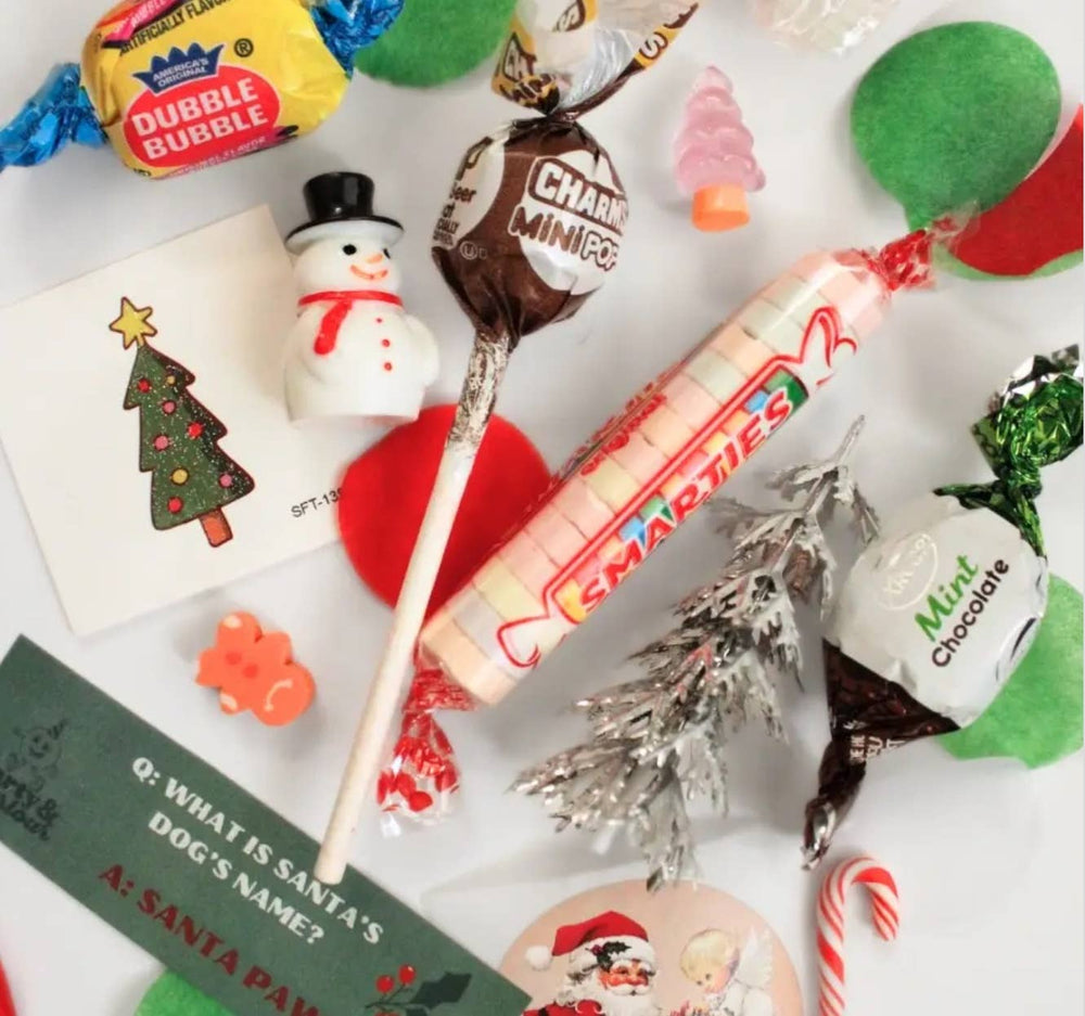 Close-up of bon bon treats: retro candies, a lollipop, a mini snowman, a tiny tree, and a printed joke card for Christmas