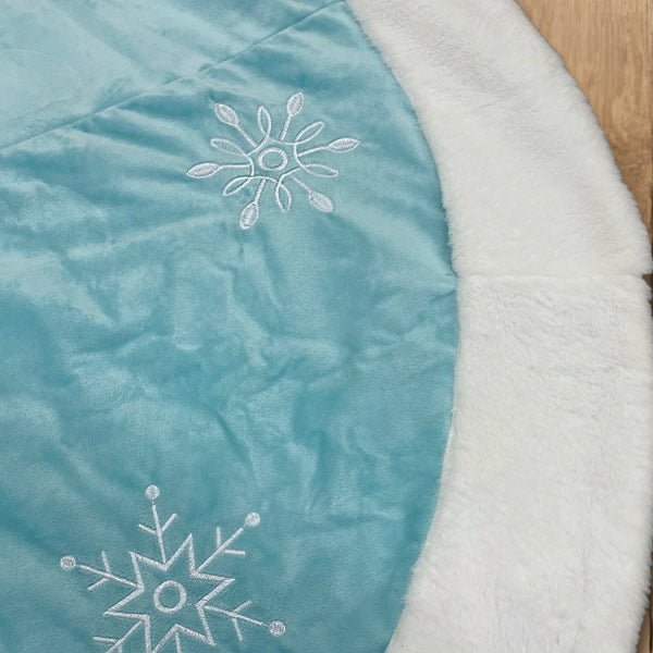 Close-up of white snowflake embroidery on pastel blue fabric beside the faux fur border