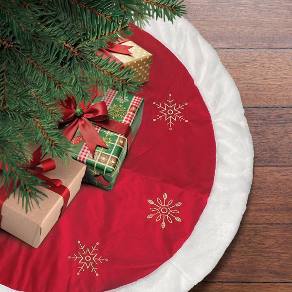 Red snowflake tree skirt under a Christmas tree with wrapped gifts on a wood floor