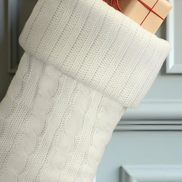 Close up of the white cable knit pattern and fold-over cuff with a gift peeking out the top