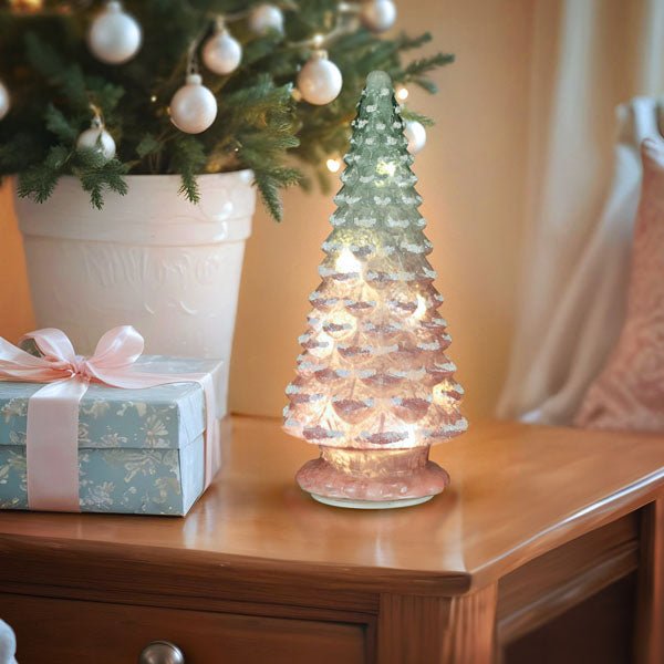 Lit pink glass tabletop tree on a wood side table beside a wrapped gift