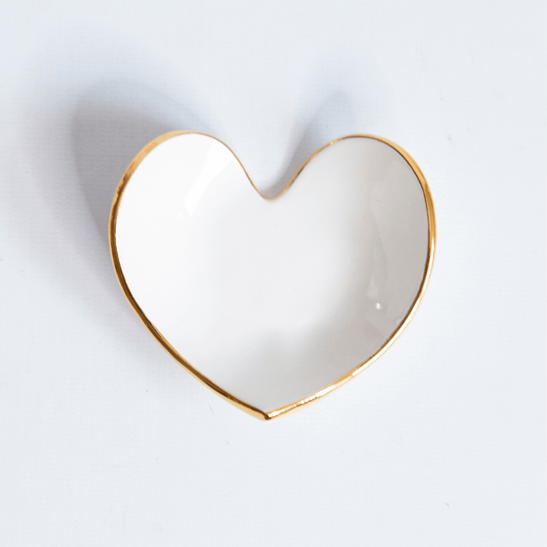 Close view of a white heart ring dish with a gold rim on pale gray