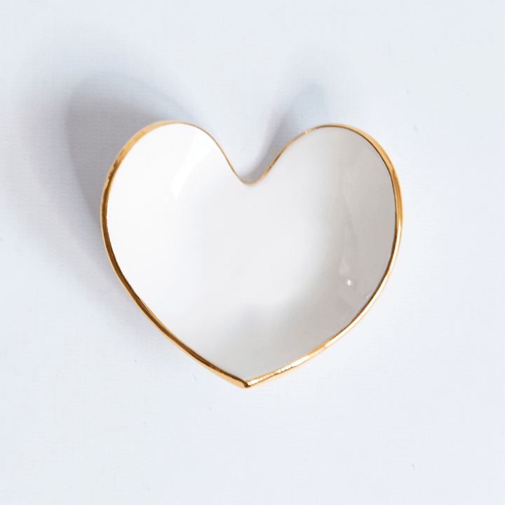 Close view of a white heart ring dish with a gold rim on pale gray