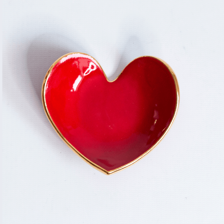 Close view of a glossy red heart ring dish with a gold rim