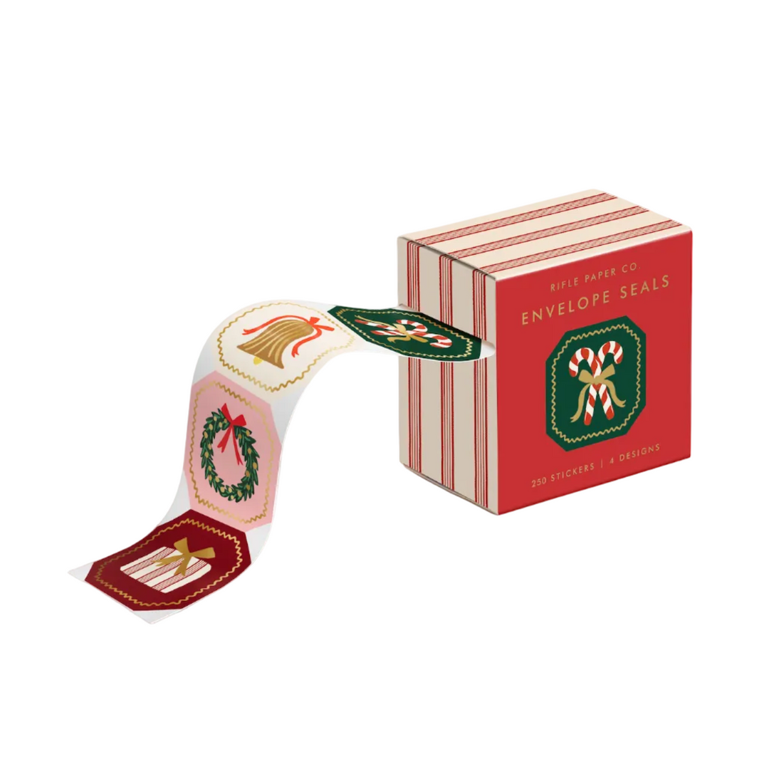 Roll of Holly Jolly Christmas envelope seals with gold foil bell, wreath, and candy cane designs beside striped box