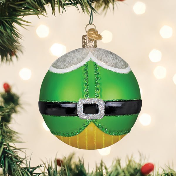 Green elf ball ornament hanging on a lit Christmas tree with warm bokeh lights
