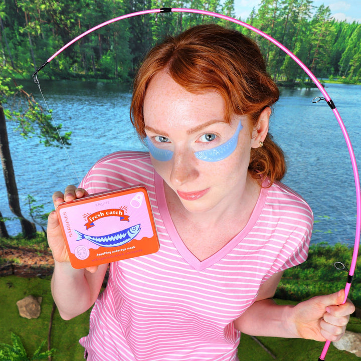 Model holding the Fresh Catch tin beneath a pink fishing rod arch with lake scenery, a whimsical summer party favor