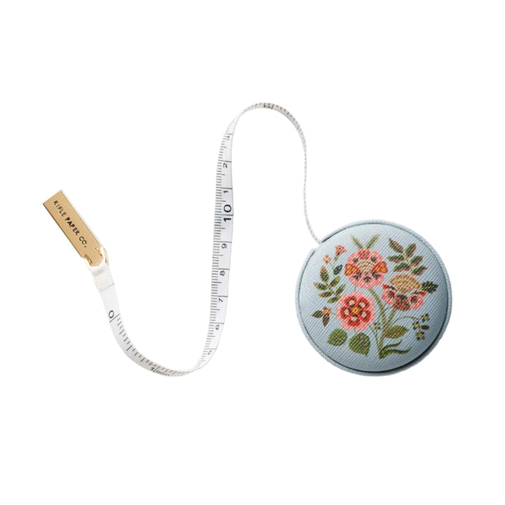 Gracie retractable measuring tape extended, light blue floral case with brass pull and Rifle Paper Co end tab