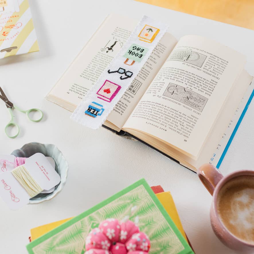 Bookish cross stitch bookmark marking a page in an open vintage stitching book