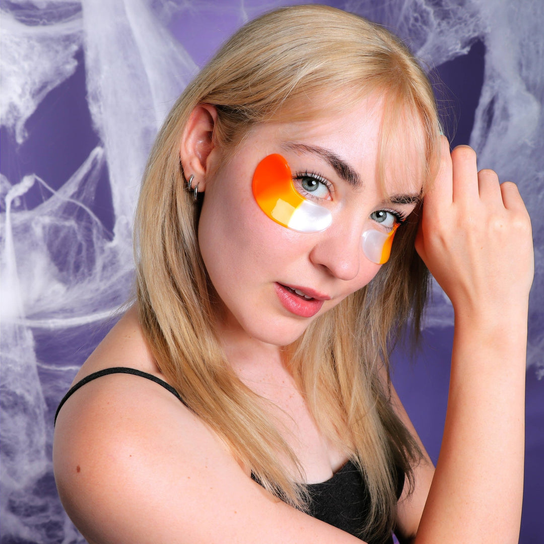 Close up of a glossy candy corn under eye patch on a model with a purple cobweb backdrop for spooky season