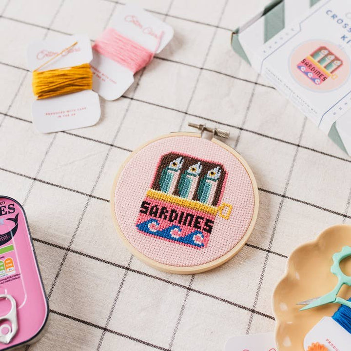 Sardines cross stitch hoop on grid tablecloth with pink and gold embroidery thread