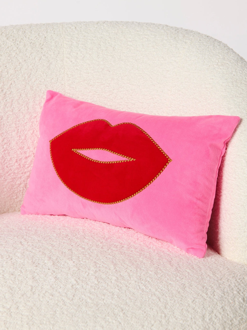 Pink lip pillow tucked into a textured cream armchair, close view of the gold beaded lip outline