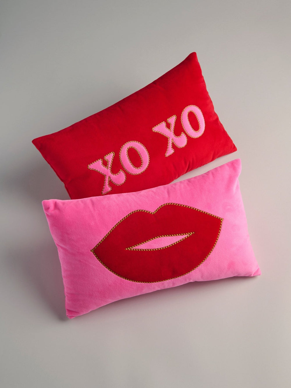 Red XO XO pillow stacked on a pink pillow with red lips on a gray backdrop, styled Galentine's decor