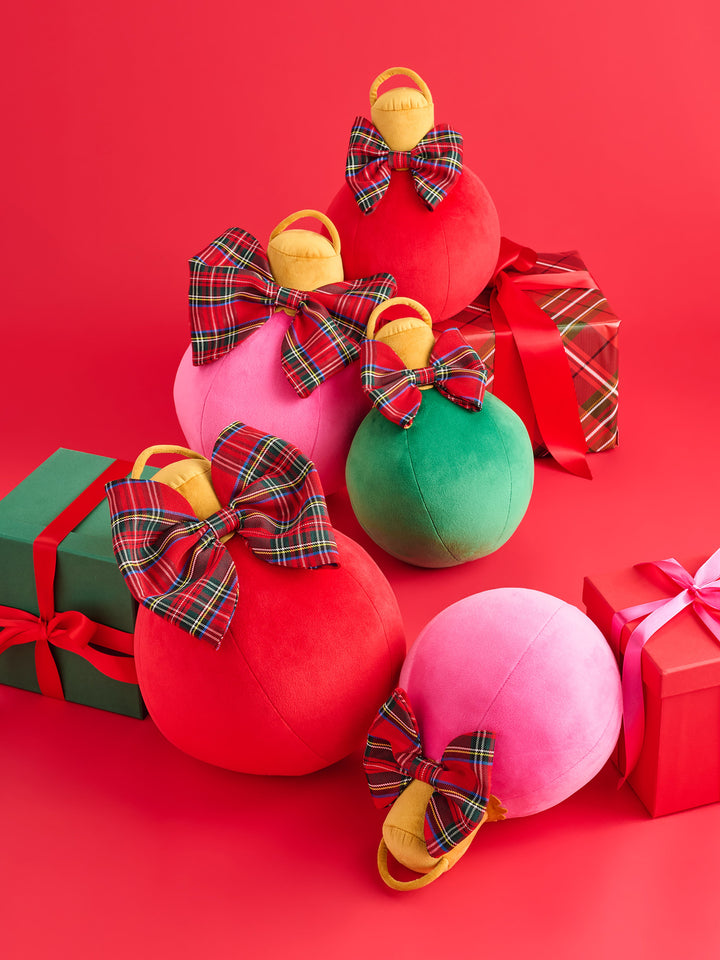 Pink and red ornament pillows with tartan bows beside wrapped gifts on red