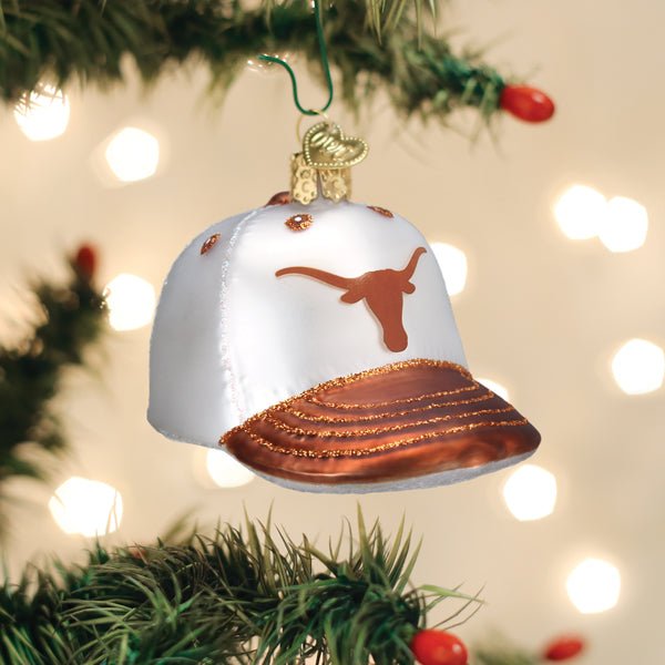 White and burnt orange Texas cap ornament hanging on a lit Christmas tree with warm bokeh
