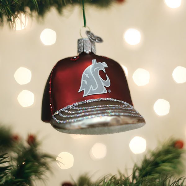 Crimson Washington State Cougars cap ornament hanging on a lit Christmas tree with soft bokeh behind
