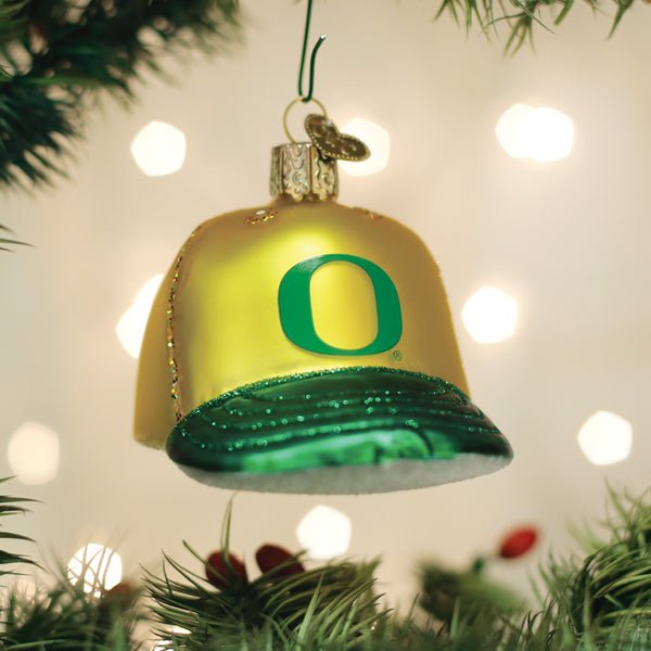 Yellow and green Oregon Ducks cap ornament hanging on a Christmas tree with warm bokeh lights