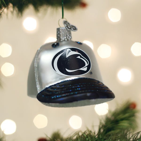 White Penn State Nittany Lions cap ornament hanging on a lit Christmas tree with soft bokeh behind