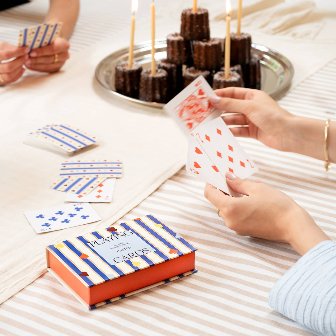 Friends playing cards around a dessert tray with candles, the boxed set styled for festive entertaining
