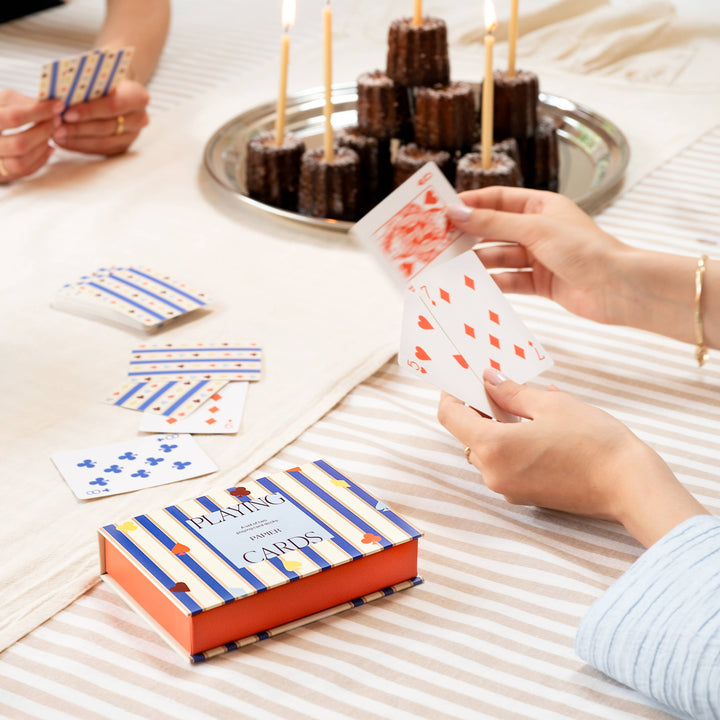 Friends playing cards around a dessert tray with candles, the boxed set styled for festive entertaining