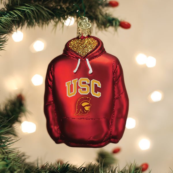USC hoodie Christmas ornament hanging on a pine branch with warm holiday lights behind