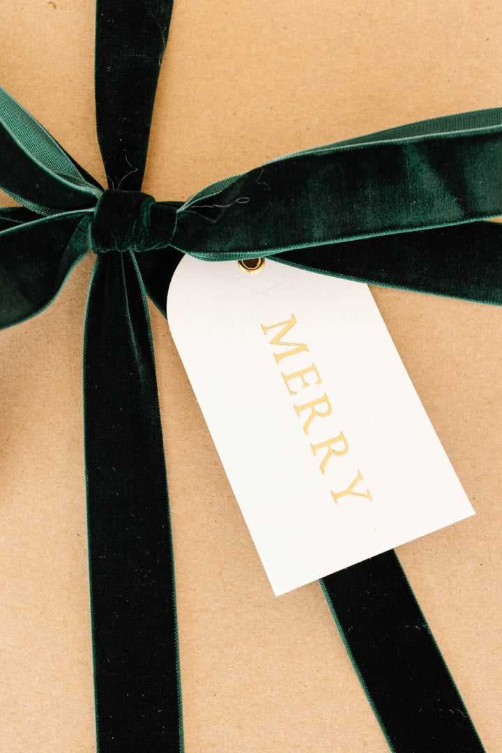 Arch gold foil MERRY tag on kraft wrapping with a deep green velvet bow