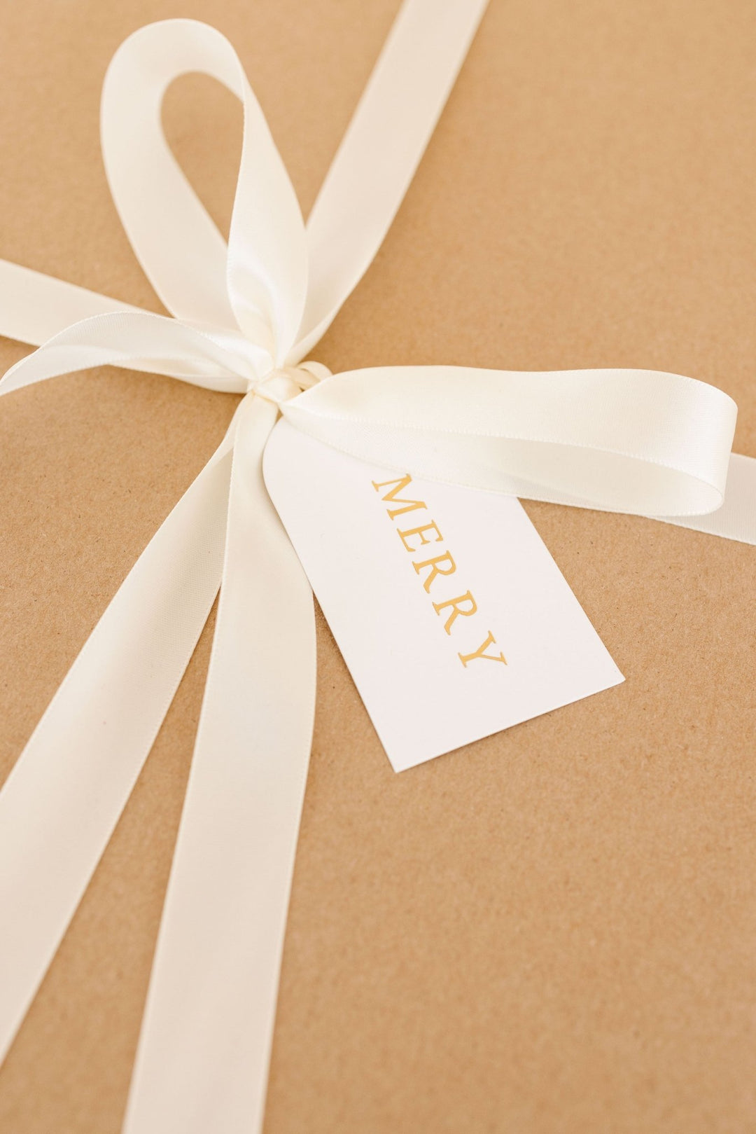 Arch letterpress tag tied with cream satin ribbon on a kraft paper present