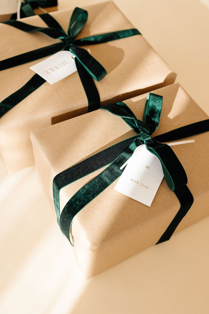 Two kraft paper gifts tied with green velvet ribbon and arch letterpress tags