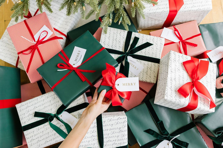 Hand placing a gift with an arch Merry tag into a pile of red and green wrapped presents