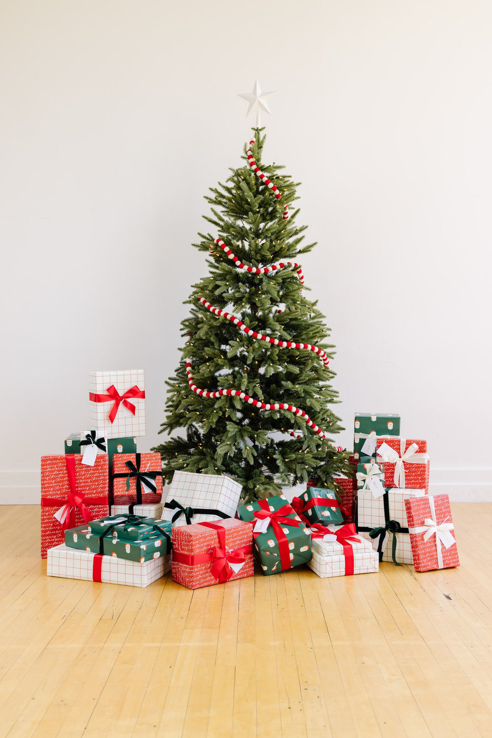 Christmas tree in a bright white room with Santa print, grid, and red script gifts piled beneath