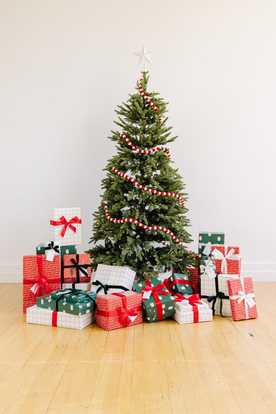 Christmas tree in a bright white room with Santa print, grid, and red script gifts piled beneath
