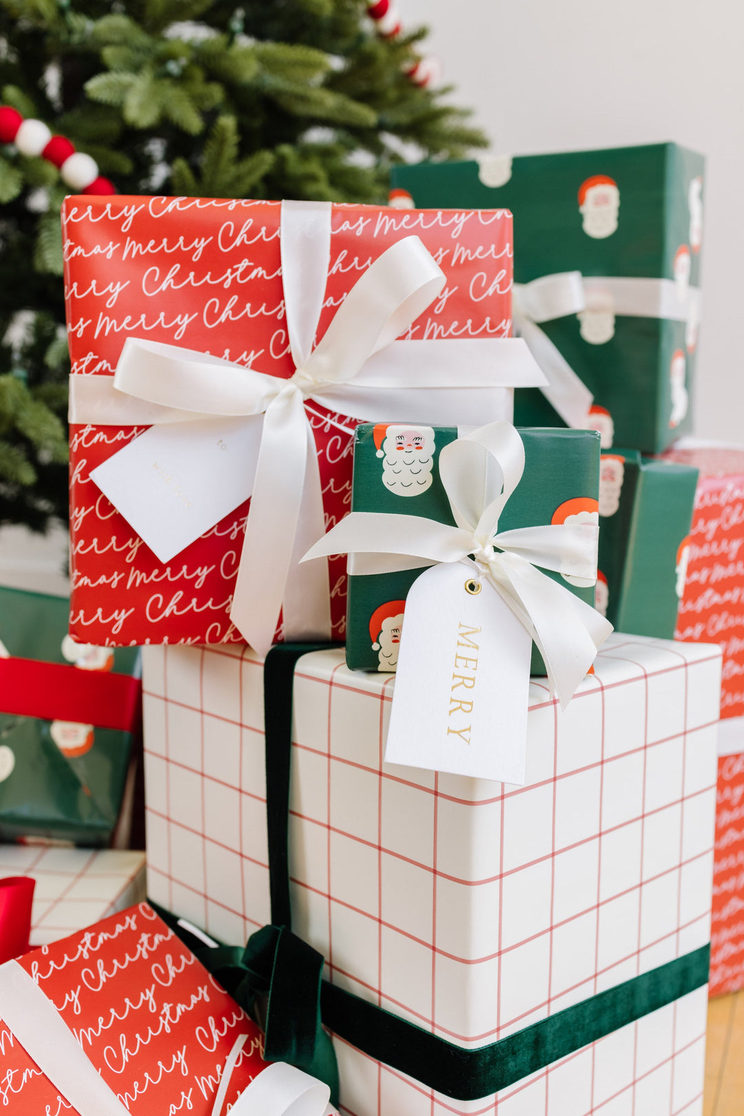 Red script and red grid gifts stacked by the tree, finished with cream satin and arch Merry tags