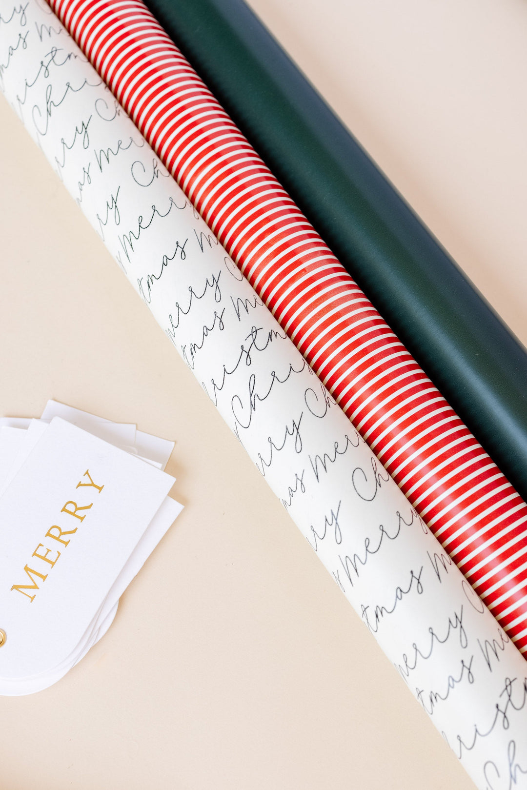 Wrapping paper rolls in white script, red stripe, and dark green beside arch letterpress Merry tags