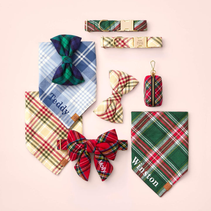 Plaid dog collars, bows, personalized bandanas, and a red tartan waste bag holder arranged on pale pink.