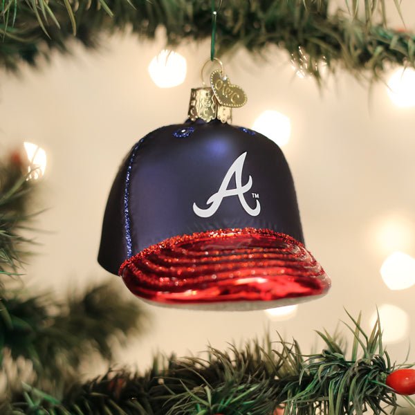 Braves cap ornament hanging on a lit Christmas tree with warm glowing bokeh lights behind