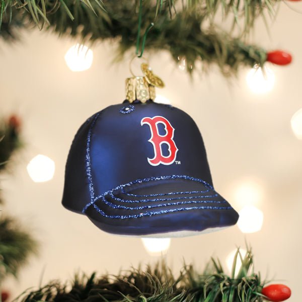 Boston Red Sox cap ornament hanging on a lit Christmas tree with warm bokeh lights and pine branches